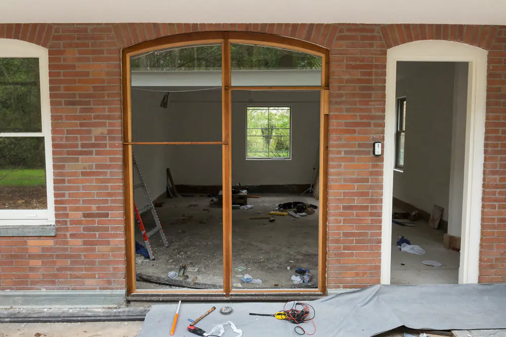 Een oud houten kozijn wordt uit de baksteengevel van een woning gehaald