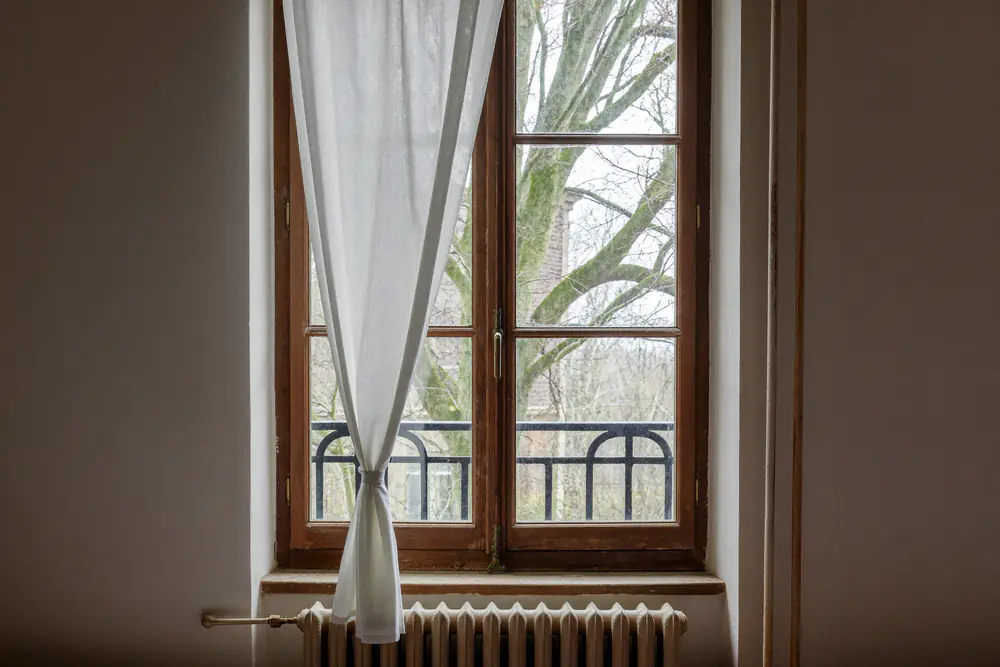 Woonkamer van een oude woning met een enkelglas houten raam en een radiator eronder