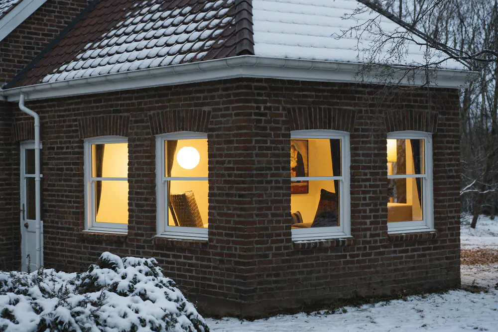 Baksteenwoning in de winter met licht sneeuw en verlichte ramen in de avond
