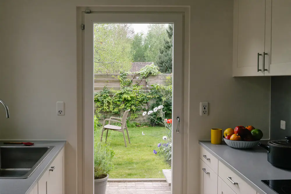 Achterdeur met glas en wit kozijn tussen een keuken en een kleine tuin