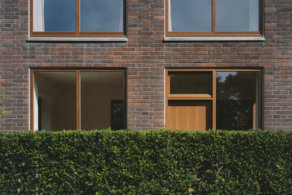 Baksteenwoning met ramen in kozijnen met een warme eikenhoutlook en een haag ervoor