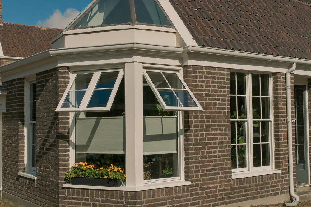 Hoek van een baksteenwoning met nieuwe witte kunststof kozijnen met draaikiepramen